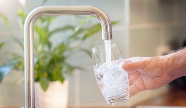 Close-up of hand holding a glass under a tap and filling it with water.